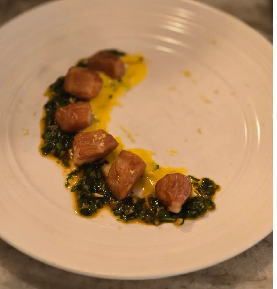 Smoked bay scallops arranged in a curved line with greens and golden sauce.