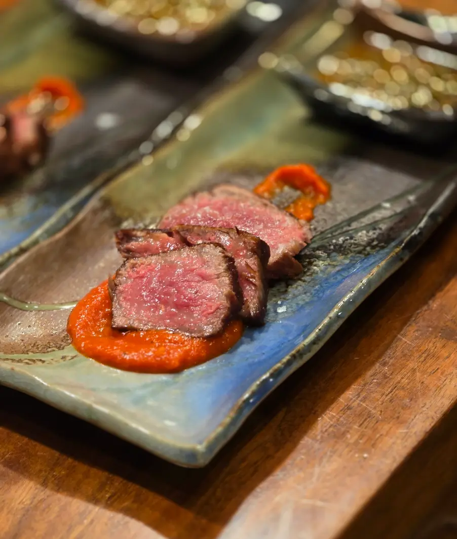 Slices of A5 Wagyu beef over red pepper sauce on a rectangular plate.