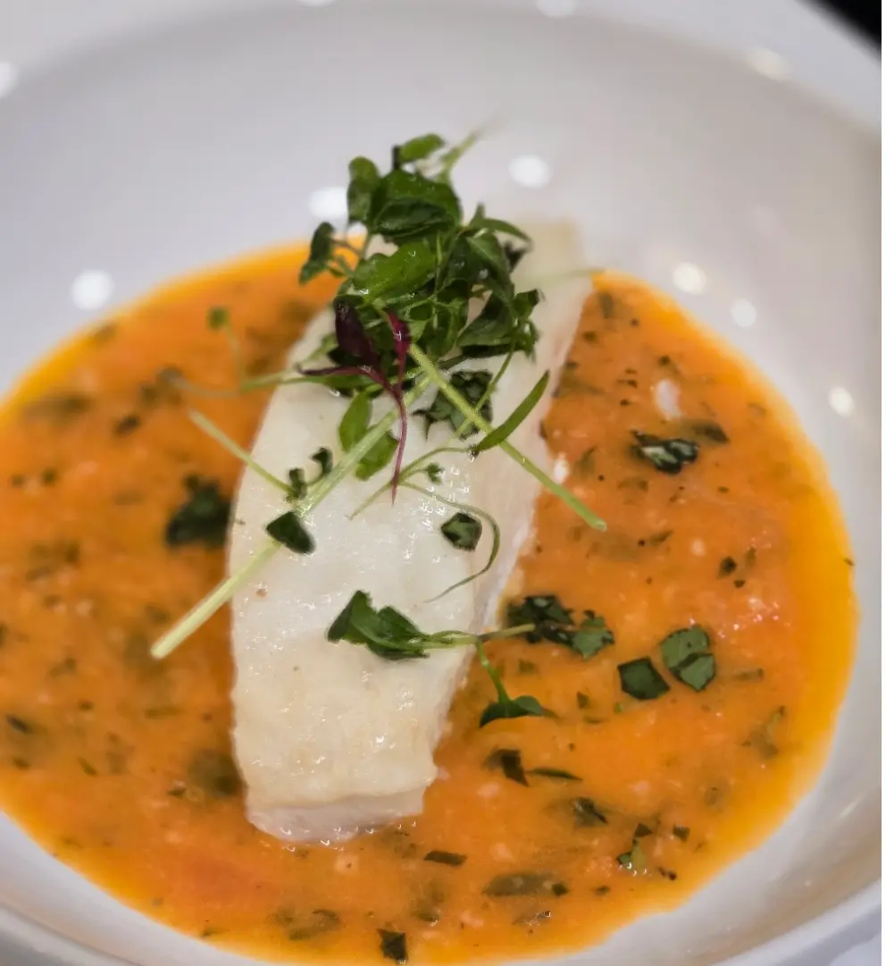 A sea bass fillet topped with microgreens in an orange herb sauce.