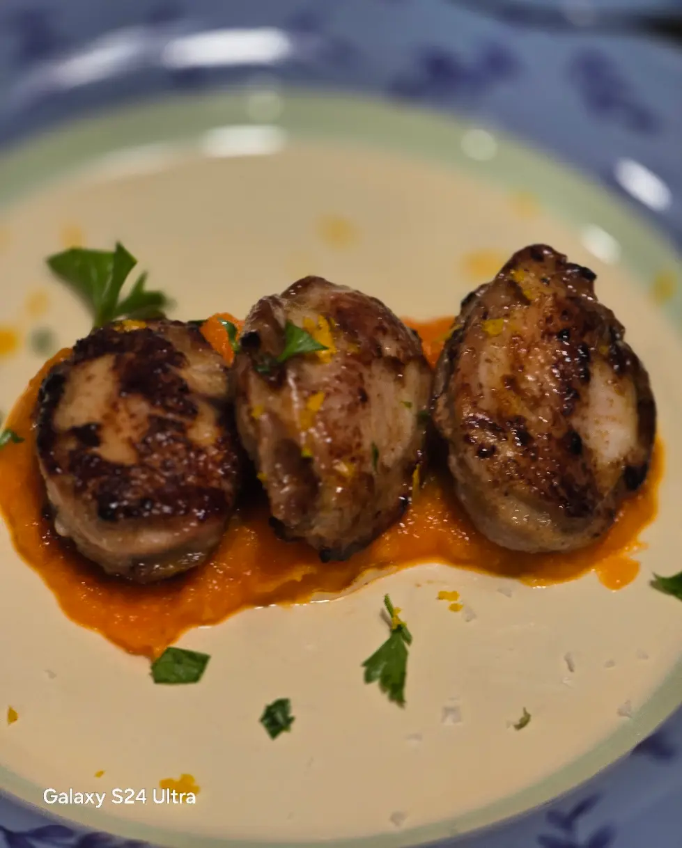 Three browned quail breast portions arranged over orange sauce.