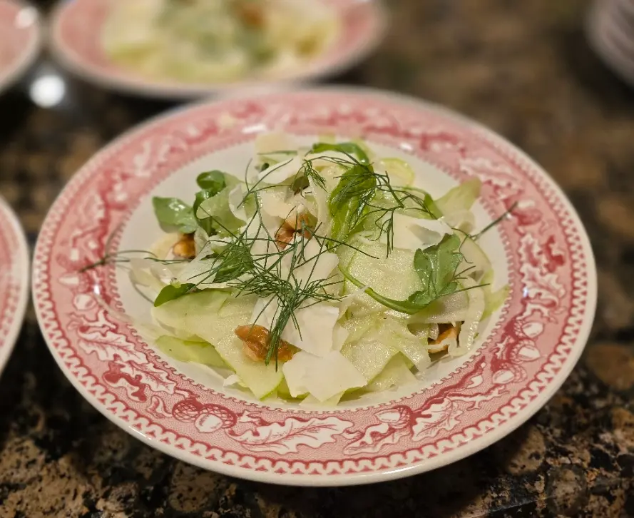 Thinly sliced fennel and apple salad with herbs on a patterned plate.