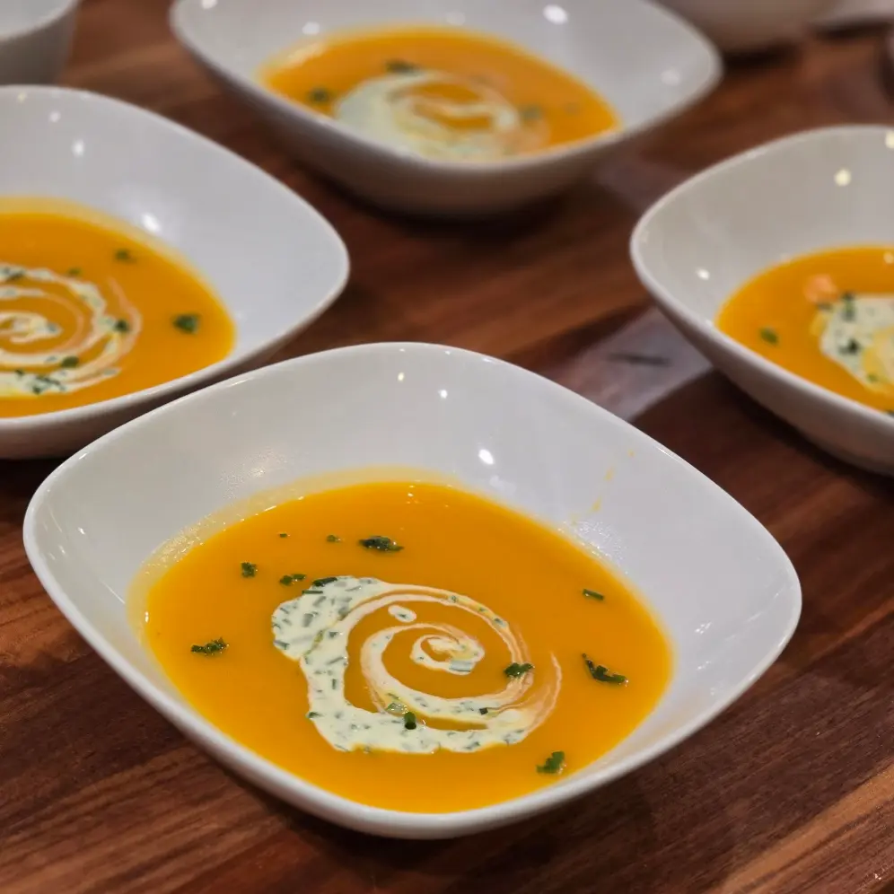 Butternut squash soup topped with a swirl of chive creme fraiche in square white bowls.
