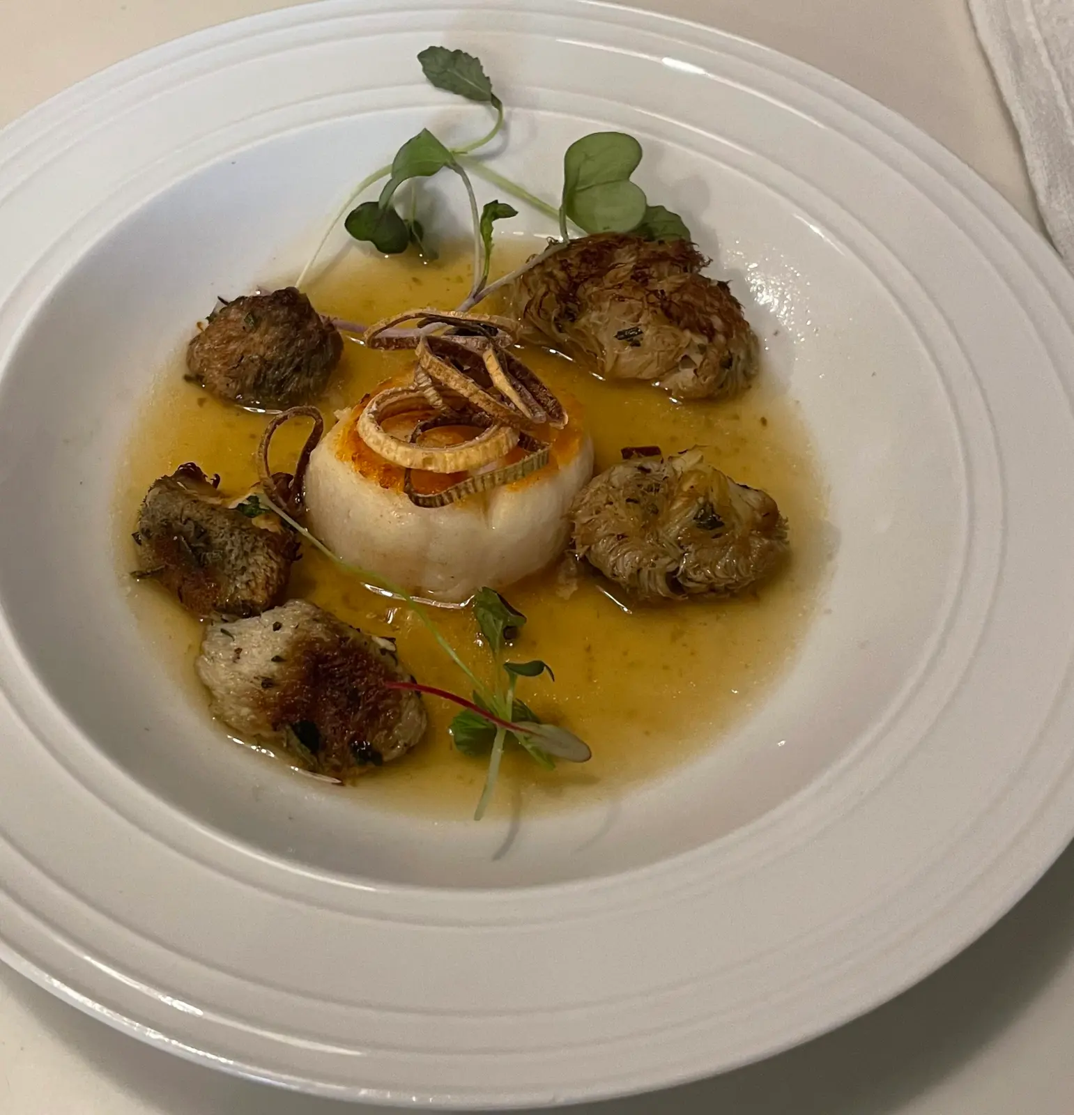A seared sea scallop surrounded by browned vegetables, sauce and microgreens.