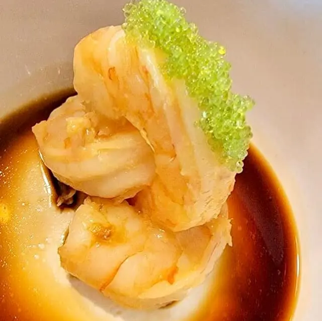 Garlic and ginger shrimp arranged upright in a dark sauce with green garnish.