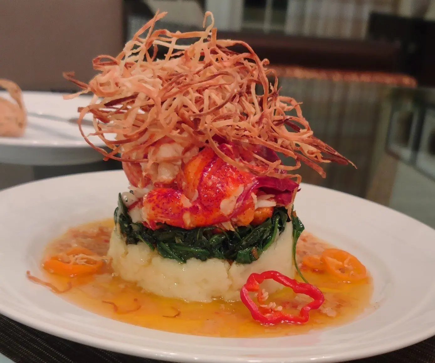 Butter-poached lobster over a layered vegetable base topped with crisp strands.