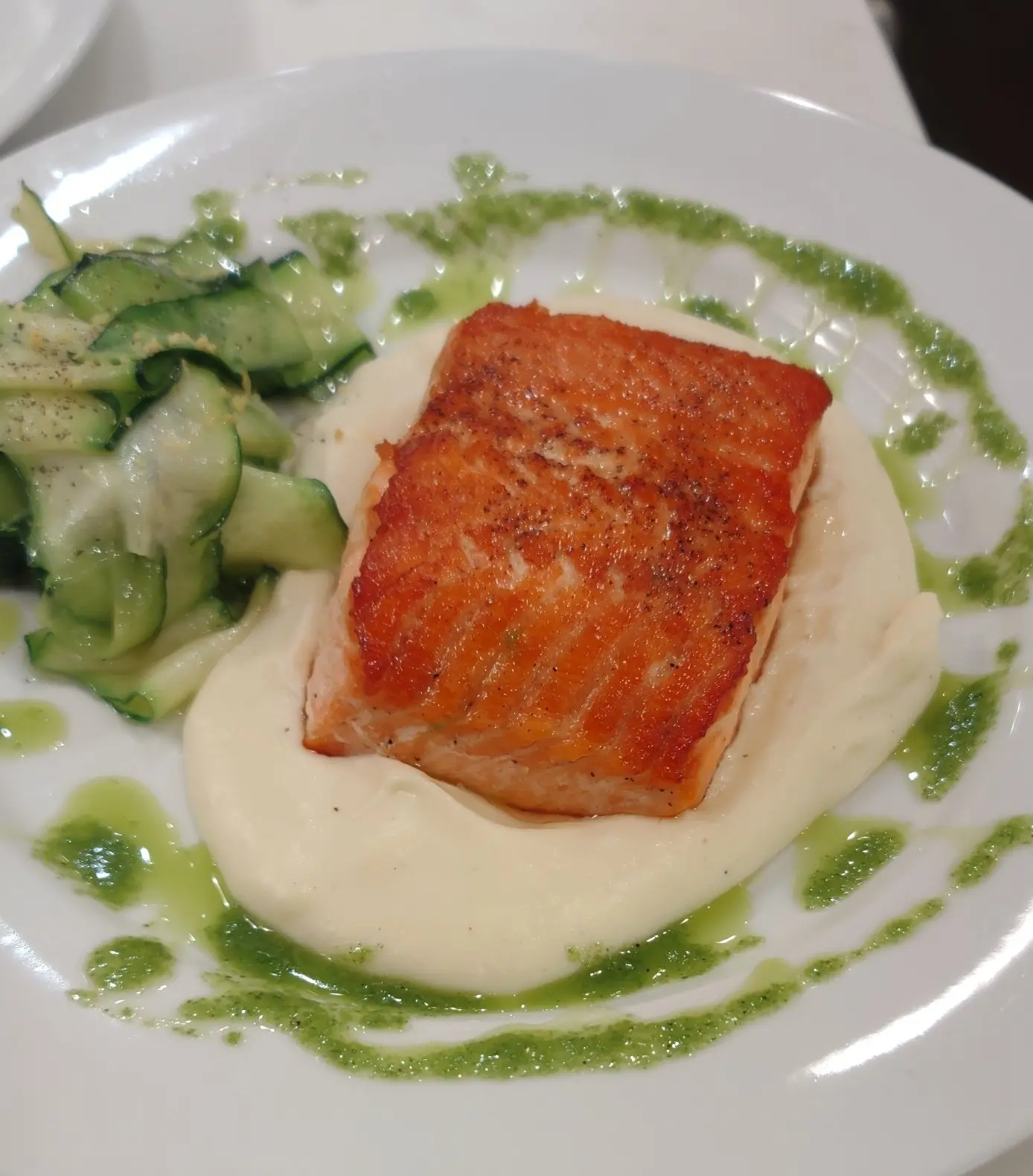 Seared salmon on a pale puree with cucumber and green sauce.
