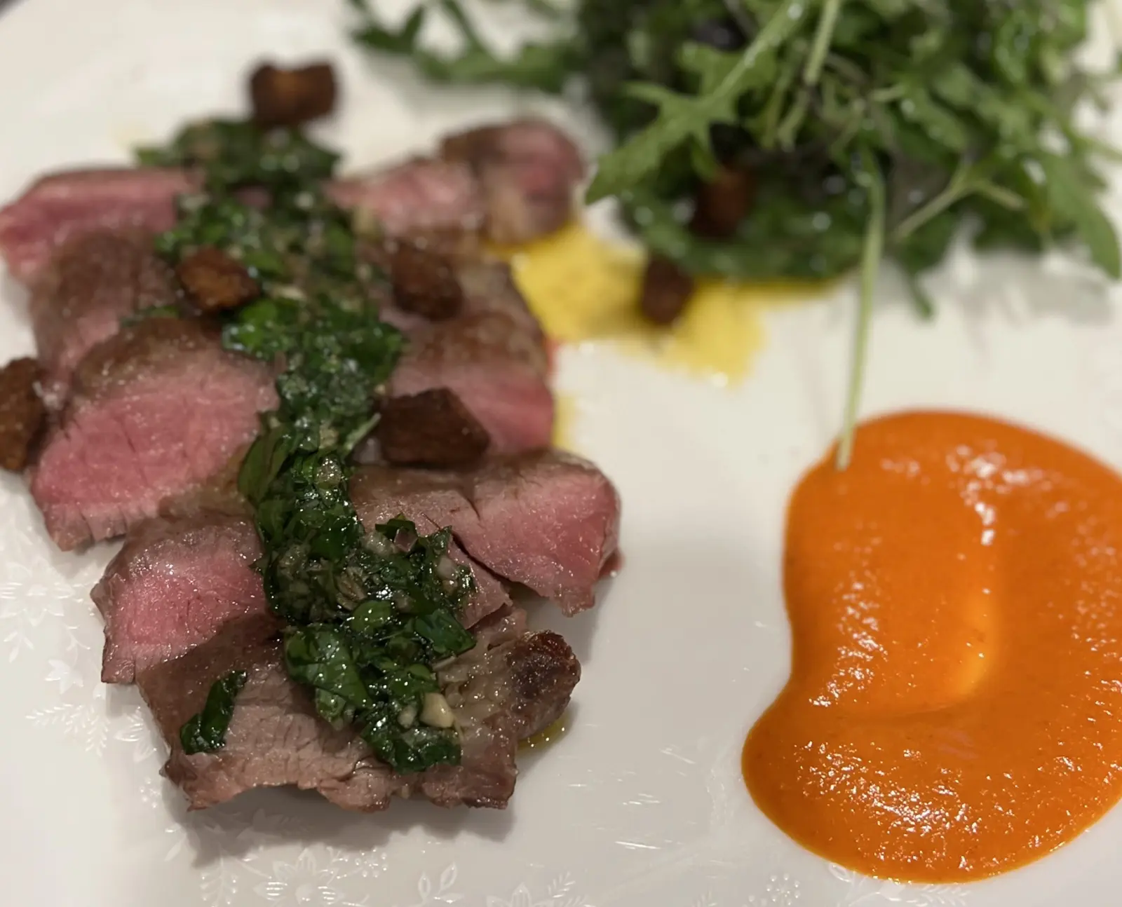 Sliced seared Iberico pluma with green herb sauce, puree and a leafy salad.