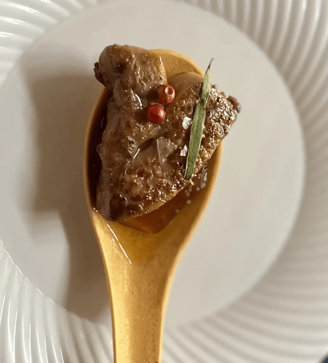 A foie gras amuse-bouche served on a wooden tasting spoon with a delicate garnish.