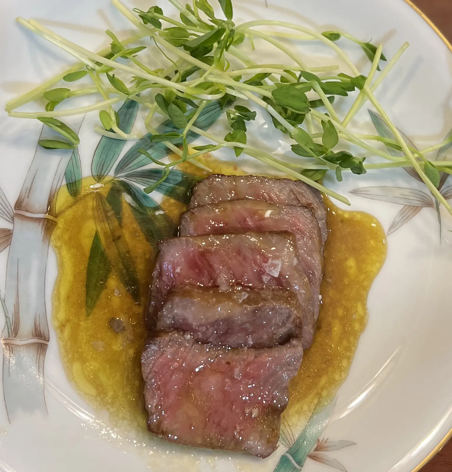 Sliced Japanese A5 Wagyu over yellow puree with a fresh microgreen salad.