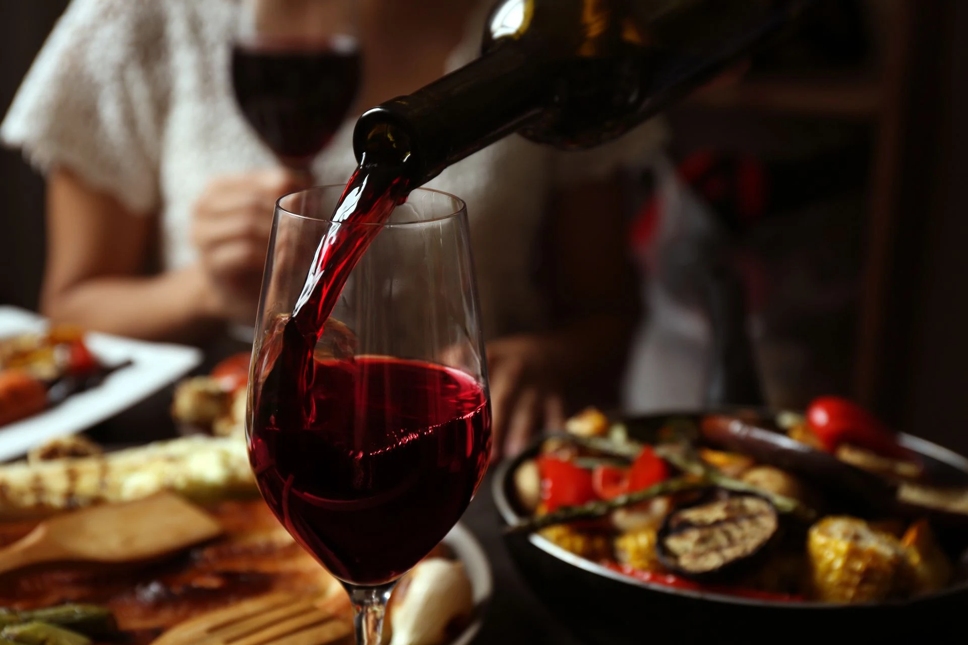 Red wine being poured into a glass beside a plated dinner.