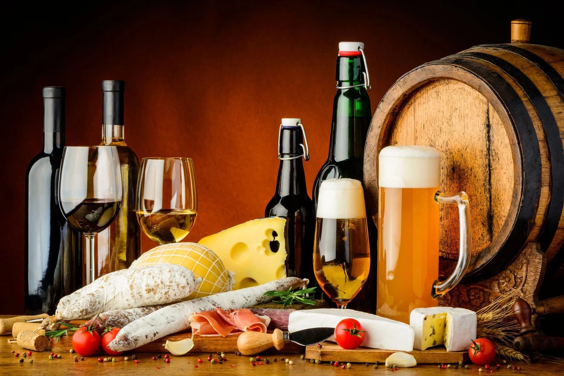 Wine, beer and spirits arranged with cheeses, bread and a small wooden barrel.