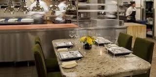 A chef's table set beside an open kitchen where chefs prepare a meal.