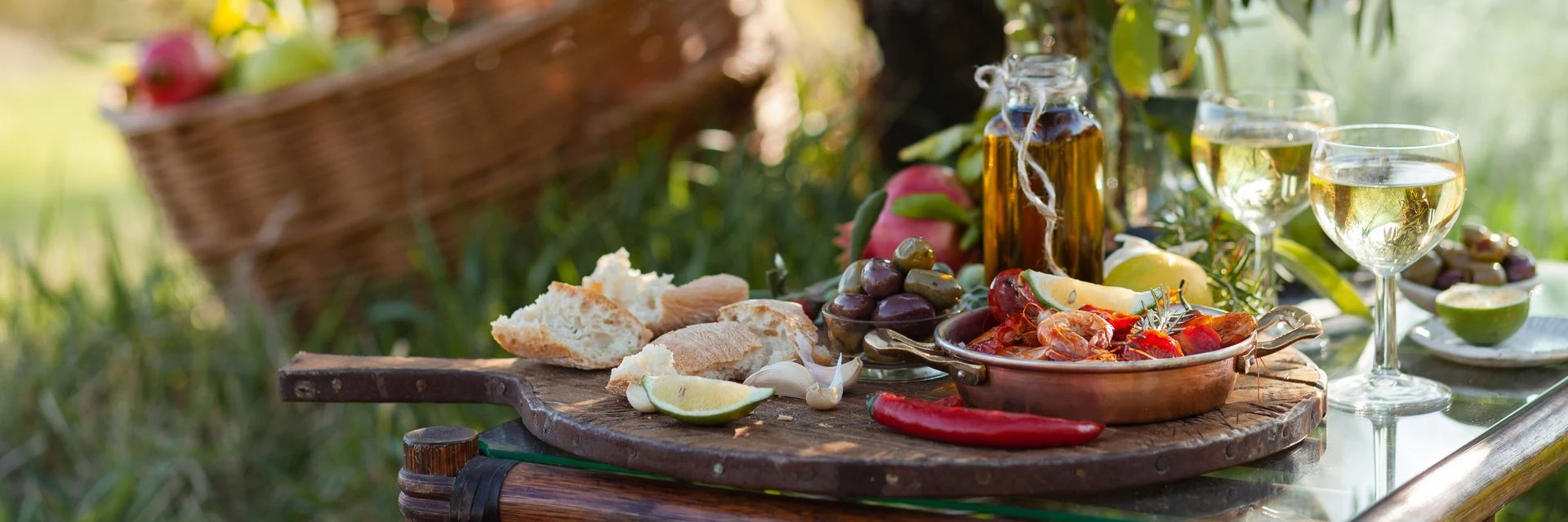 Farm-to-table produce, cheeses and wine arranged on an outdoor table beside a garden.