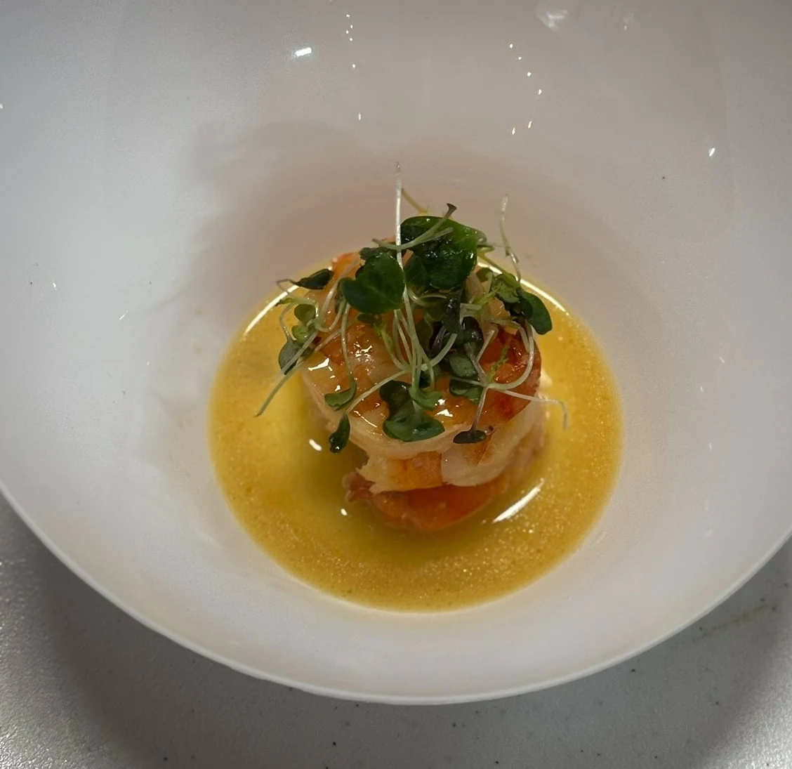 Wild-caught shrimp plated with yellow sauce and microgreens.