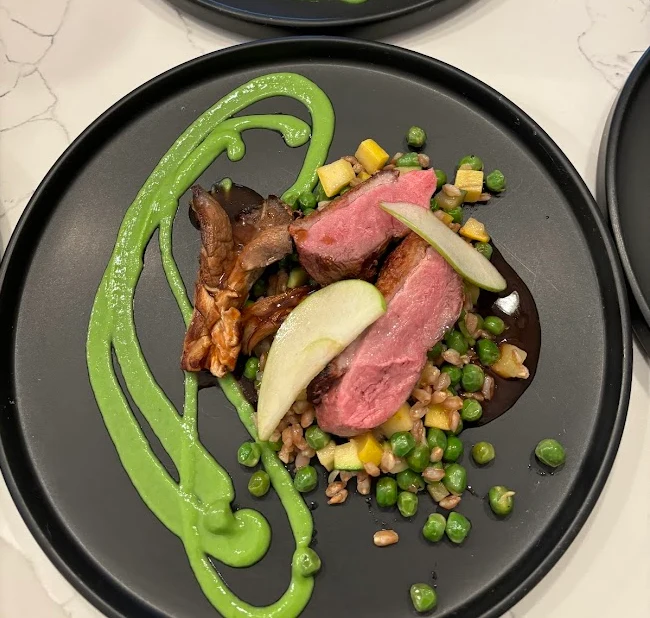 Duck breast with spring peas, mushrooms and green puree on a dark plate.
